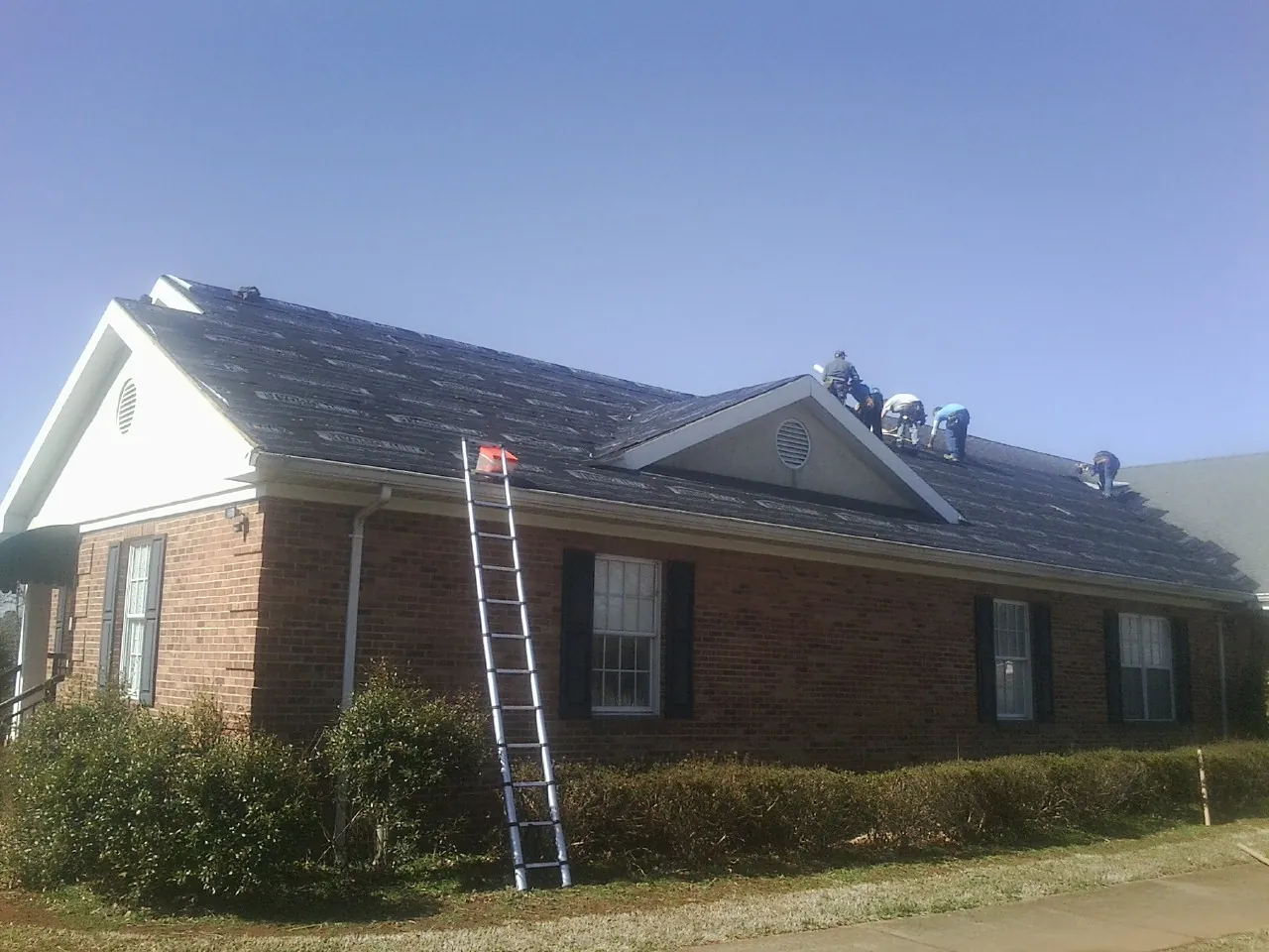 Crew tearing shingles off a brick ranch roof with a ladder set — Metal Roof Repair work by our crew in Buena Vista